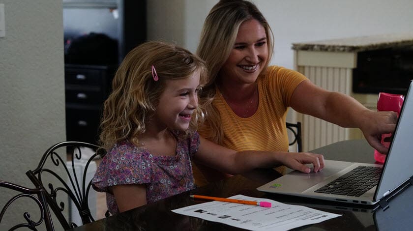 A mother and her dauther are pointing at a computer screen during an online lesson